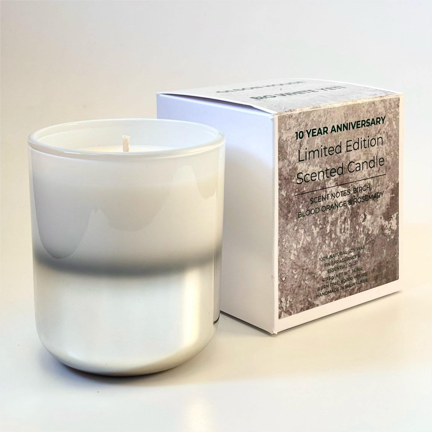 White & silver candle with a branded box on a light background