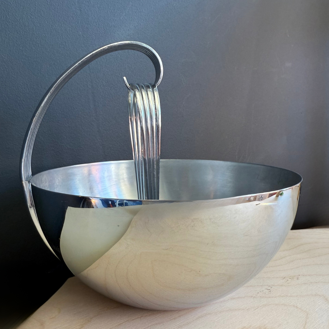 Metallic bowl with a handle on a wooden surface against a dark background