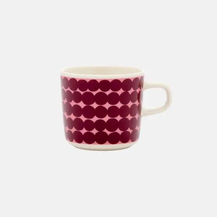 A white ceramic coffee mug featuring a bold pattern of dark red with a pink background, set against a plain light gray background.