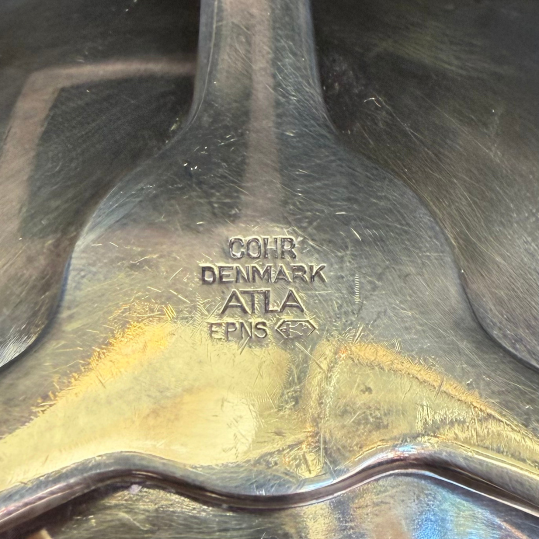 Close-up of a silver candle holder with 'Cohr Denmark' branding on a dark background