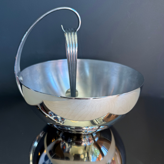 Silver bowl with handle and fork on a reflective surface