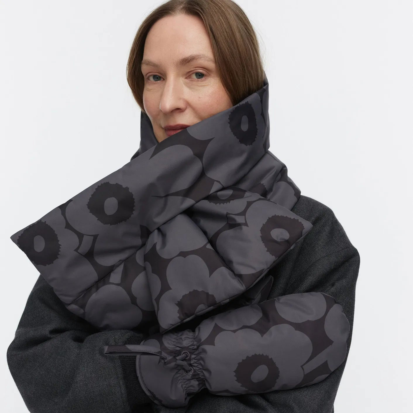 Person wearing a dark gray patterned scarf and coat on a white background