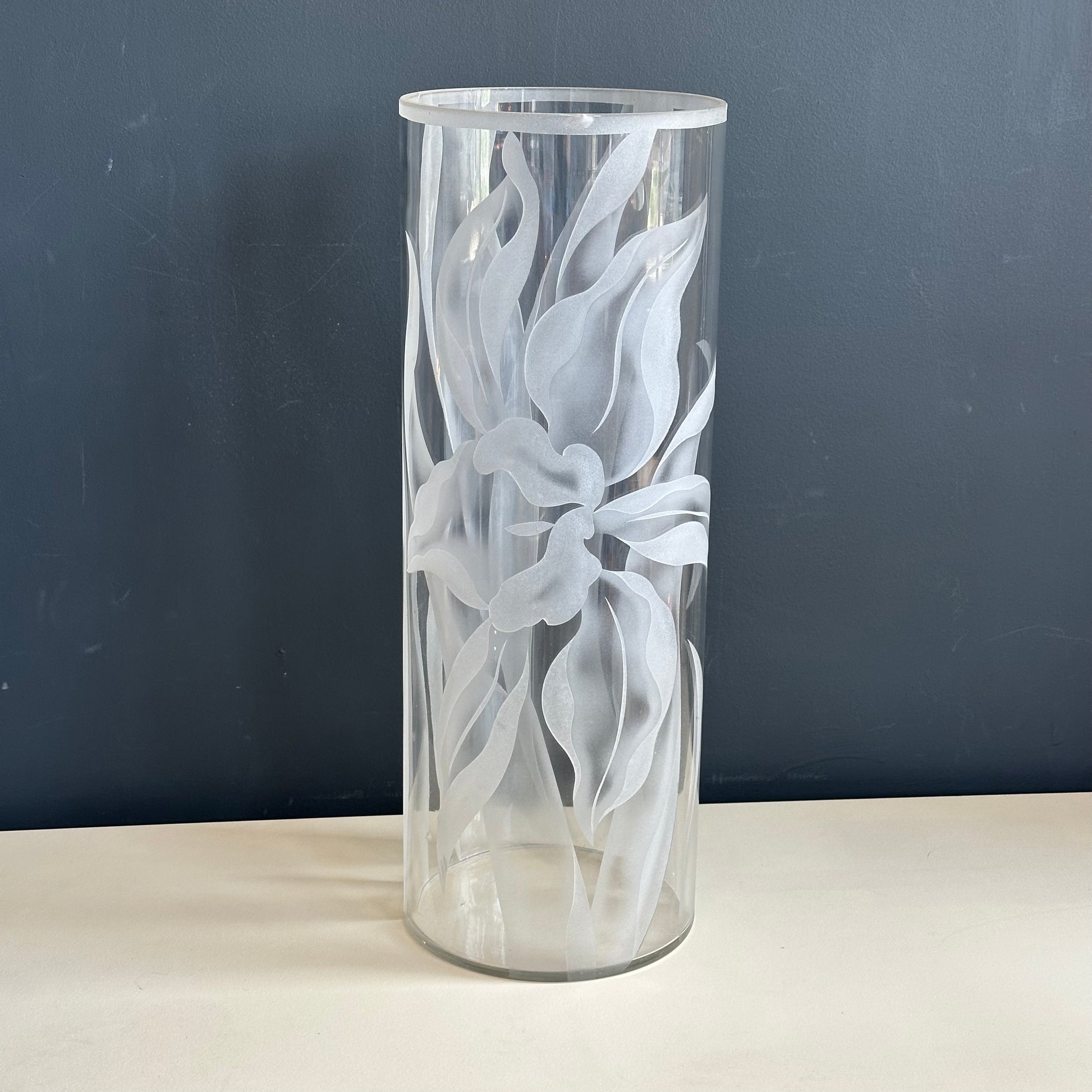 Cylindrical glass vase with floral etching on a dark background