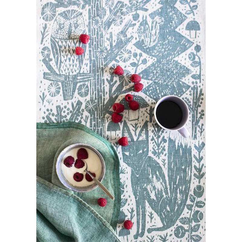Tea towel with fox and owl pattern. There is a cup of coffee and a bowl of yogurt with berries.