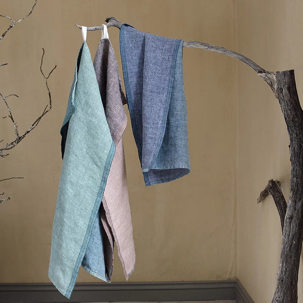 Three colored linen hand towels draped over a tree branch.