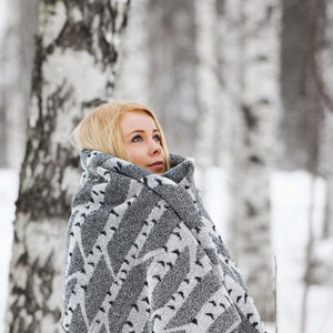 Woman wrapped in a cozy birch patterned bath towel. She is surrounded by birch trees and snow.