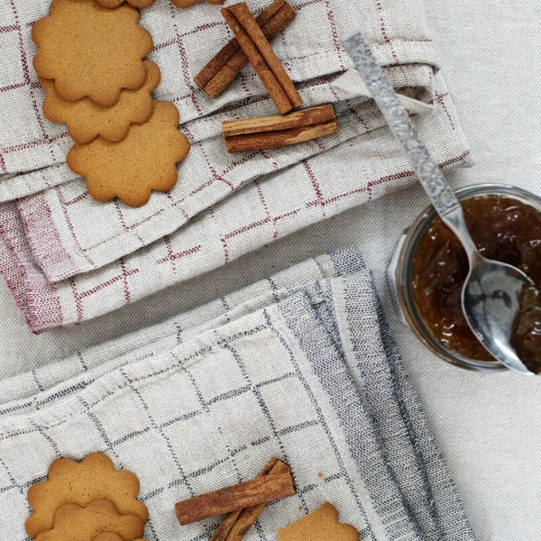 Two towels with geometric box pattern, cookies, cinnamon sticks, and a jar of jam.