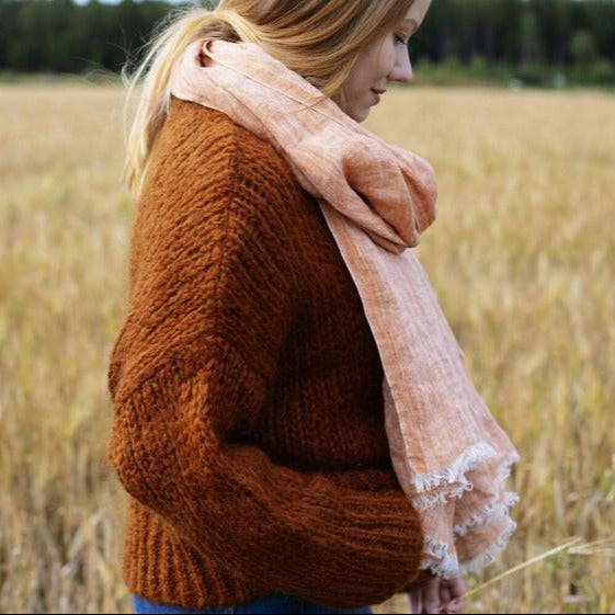 Woman in a cozy brown sweater wearing a linen scarf, and walking in a field.