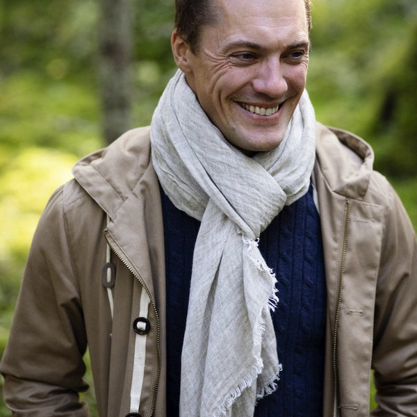 Man wearing a linen scarf and tan windbreaker with a big smile.