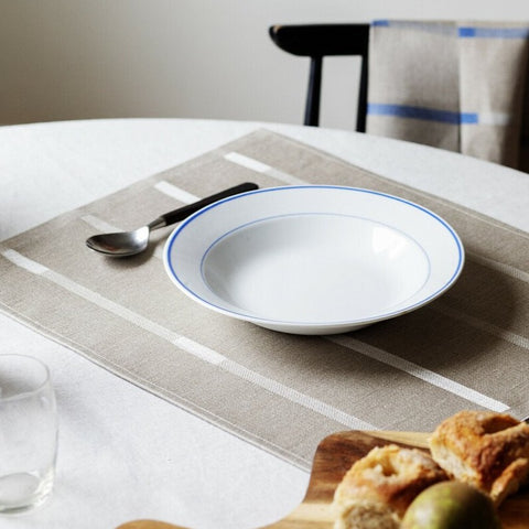 Placemat on dining table with spoon, bowl, and pastries.