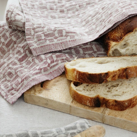 Cutting board with sliced loaf of bread wrapped in a towel.
