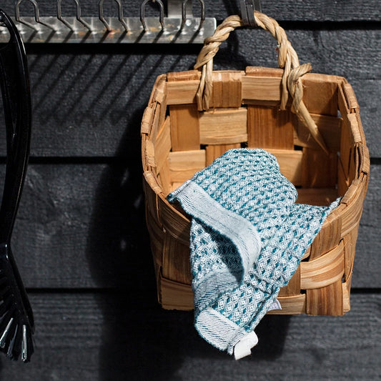 Basket hanging on a black wall with a blue dishcloth..