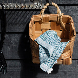 Basket hanging on a black wall with a blue dishcloth.. 