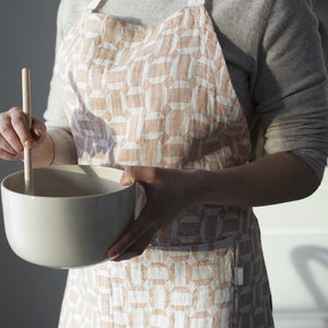 Woman wearing a patterned apron holding a mixing bowl and spoon. 